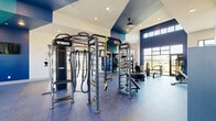 This modern fitness center in Huntsville, Alabama offers a comprehensive, single-floor workout facility designed to accommodate a wide range of training styles. The space is defined by soaring ceilings, bold navy and teal accent walls, and large floor-to-ceiling windows that flood the interior with natural light and provide open views of the surrounding landscape.

The main strength and functional training area is anchored by a multi-station TKO cable and power rack system, complete with battle ropes, TRX suspension trainers, a heavy bag, and a tire sled. A full dumbbell rack lines one wall alongside a large mirror, offering ample free weight options. Specialty equipment, including a sled push trainer and a mini trampoline, supports a variety of functional fitness routines.

A dedicated cardio zone features multiple Spirit treadmills, elliptical trainers, a stair climber, and a stationary cycle, all positioned along the windowed walls to maximize outdoor views during workouts. Adjacent to this area is an open studio space with hardwood-style flooring, track lighting, and large windows — ideal for stretching, yoga, or group exercise.

The facility also includes a water fountain station, a ceiling fan for ventilation, full-length mirrors throughout, and rubber sport flooring in the primary workout zones. Recessed lighting complements the natural light, ensuring a bright and energizing environment throughout the day.