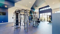 This modern fitness center in Huntsville, Alabama offers a comprehensive, single-floor workout facility designed to accommodate a wide range of training styles. The space is defined by soaring ceilings, bold navy and teal accent walls, and large floor-to-ceiling windows that flood the interior with natural light and provide open views of the surrounding landscape.

The main strength and functional training area is anchored by a multi-station TKO cable and power rack system, complete with battle ropes, TRX suspension trainers, a heavy bag, and a tire sled. A full dumbbell rack lines one wall alongside a large mirror, offering ample free weight options. Specialty equipment, including a sled push trainer and a mini trampoline, supports a variety of functional fitness routines.

A dedicated cardio zone features multiple Spirit treadmills, elliptical trainers, a stair climber, and a stationary cycle, all positioned along the windowed walls to maximize outdoor views during workouts. Adjacent to this area is an open studio space with hardwood-style flooring, track lighting, and large windows — ideal for stretching, yoga, or group exercise.

The facility also includes a water fountain station, a ceiling fan for ventilation, full-length mirrors throughout, and rubber sport flooring in the primary workout zones. Recessed lighting complements the natural light, ensuring a bright and energizing environment throughout the day.