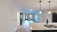 Located at 316 Main St in Hamilton, Ohio, this well-appointed single-floor residence offers three bedrooms, two bathrooms, and a thoughtfully designed layout. The open-concept kitchen and living area serves as the heart of the home, anchored by a large granite-topped island with a double stainless steel sink and pendant lighting overhead. Dark cabinetry provides a striking contrast against the light stone countertops, while stainless steel appliances complete the modern kitchen. Wood-look flooring flows throughout the main living and kitchen areas, adding warmth and continuity.

The living room is bright and airy, benefiting from natural light through windows and a glass-panel exterior door. Neutral wall tones carry throughout the home, creating a calm and cohesive atmosphere. The bedrooms offer plush carpet underfoot, with the secondary bedrooms featuring closets and ample window light. The spacious primary bedroom connects to its own bathroom, which is equipped with a sleek glass-enclosed walk-in shower with tile surround and matte black fixtures. The primary suite also includes a generous walk-in closet with wire shelving for organized storage. Two hallways connect the spaces efficiently, and a dedicated utility room rounds out the functional layout of this well-designed home.