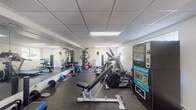 Located at 1015 Spanish River Rd in Boca Raton, Florida, this fitness center offers a comprehensive, single-floor workout facility designed to support a wide range of exercise routines. The space features a drop-panel ceiling with recessed fluorescent lighting that keeps the area well-lit throughout, while windows along the walls invite natural light and views of the surrounding greenery.

The gym is equipped with an extensive selection of cardio machines, including a treadmill, elliptical trainers, and a stationary cycle, providing ample options for aerobic workouts. A dedicated strength training area houses a multi-station cable machine, an adjustable weight bench, and a full rack of dumbbells ranging across various weight increments, accommodating both beginners and experienced lifters. Medicine balls, kettlebells, and a stability ball round out the functional fitness offerings.

Full-length mirrors line one wall, enhancing the sense of space and allowing users to monitor their form during exercises. Rubber flooring throughout provides traction and impact absorption. For convenience, snack and drink vending machines are positioned near the entrance. Glass doors open to an outdoor area flanked by tropical plants, adding a welcoming, resort-like ambiance to this well-appointed community fitness facility.