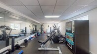 Located at 1015 Spanish River Rd in Boca Raton, Florida, this fitness center offers a comprehensive, single-floor workout facility designed to support a wide range of exercise routines. The space features a drop-panel ceiling with recessed fluorescent lighting that keeps the area well-lit throughout, while windows along the walls invite natural light and views of the surrounding greenery.

The gym is equipped with an extensive selection of cardio machines, including a treadmill, elliptical trainers, and a stationary cycle, providing ample options for aerobic workouts. A dedicated strength training area houses a multi-station cable machine, an adjustable weight bench, and a full rack of dumbbells ranging across various weight increments, accommodating both beginners and experienced lifters. Medicine balls, kettlebells, and a stability ball round out the functional fitness offerings.

Full-length mirrors line one wall, enhancing the sense of space and allowing users to monitor their form during exercises. Rubber flooring throughout provides traction and impact absorption. For convenience, snack and drink vending machines are positioned near the entrance. Glass doors open to an outdoor area flanked by tropical plants, adding a welcoming, resort-like ambiance to this well-appointed community fitness facility.