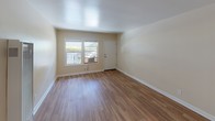 Located at 990 Palm Ave in the heart of West Hollywood, CA, this single-floor unit offers a clean, functional layout with thoughtful finishes throughout. The main living area features warm wood-look laminate flooring that runs seamlessly across the space, complemented by neutral beige walls and smooth white ceilings that enhance the sense of brightness. A large window with a window-unit air conditioner allows natural light to fill the room while providing outdoor views, and a white entry door adds a clean, welcoming touch.

The kitchen is well-appointed with stainless steel appliances, including a gas range and an over-the-range microwave. Light blue-toned walls contrast pleasantly with white cabinetry and a white countertop featuring a double stainless steel sink. A window with white horizontal blinds above the sink provides additional natural light, making the kitchen feel open and airy.

A hallway connects the living space to the bathroom, where a frosted-glass door adds a modern detail. The bathroom is finished with white subway tile surrounding a full bathtub and shower combo with chrome fixtures. A frosted window above the tub allows natural light while maintaining privacy. The space is rounded out with a pedestal sink, keeping the aesthetic simple and clean. A mirrored closet door in the hallway adds depth to the passage.