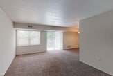 This single-floor residence offers a well-organized layout designed for comfortable everyday living. The living area is generously sized, finished with warm brown carpeting that extends throughout the space. Large windows fitted with blinds and a sliding glass door with vertical blinds flood the room with natural light and provide direct access to an outdoor balcony, where views of surrounding greenery create a pleasant, nature-adjacent atmosphere.

The kitchen is efficiently designed and features warm oak cabinetry, dark granite-style countertops, a stainless steel sink, and white tile backsplash. Appliances include a gas range and dishwasher, offering practical functionality in a compact footprint. Light tile flooring completes the kitchen's clean aesthetic.

The bedroom is a quiet, carpeted retreat with ample wall space and a standard closet with bifold doors. A separate walk-in closet provides generous storage capacity, adding to the room's practicality. A window brings in natural light, maintaining the airy feel found throughout the unit.

The bathroom is finished with white subway tile wainscoting, a full tub-shower combination, a vanity with mirror cabinet, and light tile flooring, presenting a clean and functional space. Overall, the residence offers a straightforward, comfortable layout with consistent finishes throughout.