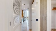 Located on Griffis Way in West Palm Beach, Florida, this thoughtfully designed 460-square-foot, one-bedroom, one-bathroom apartment delivers modern urban living with impressive style. The open living area is anchored by dramatic floor-to-ceiling windows that flood the space with natural light and offer sweeping city views. Light hardwood flooring runs throughout, complementing the clean white walls and contemporary aesthetic. A striking sputnik chandelier serves as a focal point in the living room, which comfortably accommodates a seating area and entertainment setup. The galley-style kitchen features warm wood cabinetry, white quartz countertops, stainless steel appliances including a range and over-the-range microwave, and a mosaic tile backsplash that adds texture and visual interest. A hallway connects the main living area to the private bedroom, which spans 310 square feet and offers a serene, softly lit retreat with a ceiling fan and neutral tones. The full bathroom is finished with large-format marble-style tile in the tub/shower surround, light wood vanity cabinetry, a white quartz countertop, and light wood-look flooring, creating a clean and spa-like atmosphere throughout.