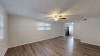 Located at 13418 Dottie Dr in Tampa, FL, this single-story 2-bedroom, 1-bathroom home offers a well-organized layout designed for comfortable everyday living. The living room serves as the heart of the home, featuring warm wood-look laminate flooring, crown molding, a textured ceiling, a ceiling fan with light fixture, and multiple windows fitted with blinds that allow ample natural light to fill the space. A front entry door with a transom window adds a welcoming touch.

The galley-style kitchen is a standout feature, equipped with rich dark espresso cabinetry, light granite-style countertops, stainless steel appliances including a range, microwave, and refrigerator, and a window above the sink. A back door provides convenient exterior access directly from the kitchen.

Both bedrooms continue the wood-look flooring theme and include ceiling fans and windows with blinds for natural light and ventilation. The primary bedroom offers a closet, while the second bedroom features a wide sliding double-door closet. The full bathroom includes a tub-shower combination with white tile surround and a privacy window.

A connecting hallway ties the layout together efficiently. The home's clean, neutral palette throughout creates a bright and move-in-ready atmosphere suited for a variety of lifestyles.
