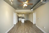 This single-floor unit blends modern finishes with industrial-inspired design elements, creating a distinctive and functional living space. The kitchen serves as a central highlight, featuring crisp white cabinetry extending to the ceiling, dark granite countertops, and a full suite of stainless steel appliances including a refrigerator, electric range, microwave, and dishwasher. A central island with a matching granite surface provides additional prep space and casual seating. Light wood-style flooring runs throughout the kitchen and entry area, adding warmth and continuity.

The bedrooms are carpeted for comfort and feature a standout architectural detail: dark-painted, corrugated metal ceilings with exposed ductwork and ceiling fans, lending an industrial loft character to the space. Large windows fill these rooms with natural light and offer views of the surrounding area.

Two bathrooms serve the unit, each finished with white cabinetry and dark granite countertops. The primary bathroom includes a wide vanity with a large mirror and a glass-enclosed shower. The secondary bathroom features a skylight, a single vanity, and a glass-enclosed shower-tub combination. Both bathrooms are finished with the same light wood-style flooring found throughout the main living areas, ensuring a cohesive aesthetic across the entire unit.