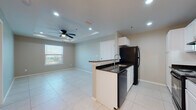 Located at 9500 S Mile One E Rd in Mercedes, Texas, this single-floor unit presents a clean, contemporary design throughout. Large-format light tile flooring runs consistently across the living spaces, contributing to a bright and cohesive aesthetic.

The kitchen is well-appointed with white cabinetry, dark granite countertops, and black appliances including a refrigerator, electric range, and dishwasher. A peninsula with an integrated sink and additional counter space separates the kitchen from the adjoining living and dining areas, creating an open, functional layout. Recessed lighting and a ceiling fan with a tray ceiling detail add character to the living space, which also benefits from a window allowing natural light to filter in.

The bedrooms feature the same tile flooring, neutral-toned walls, and tray ceilings with ceiling fans, providing a comfortable and airy feel. Each room includes window blinds for privacy and light control.

The bathroom is finished with tile flooring, a white vanity, and a tub-shower combination with built-in shelving, offering a practical and tidy space. Overall, the unit presents a well-maintained, move-in-ready interior with consistent finishes throughout.