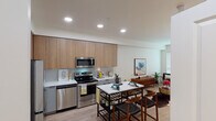 This thoughtfully designed single-floor residence offers a seamless blend of modern aesthetics and functional living. The open-concept kitchen is a standout feature, showcasing warm wood-tone upper cabinetry paired with sleek light gray lower cabinets, white quartz countertops, and a subtle tile backsplash. A full suite of stainless steel appliances — including a refrigerator, electric range, over-the-range microwave, and dishwasher — equips the space for everyday use. The kitchen flows naturally into the dining and living areas, creating an inviting, connected layout ideal for both entertaining and daily life. Light wood-style flooring runs consistently throughout, reinforcing a cohesive and contemporary feel. The bedroom is bright and comfortable, featuring a window fitted with horizontal blinds that allow for adjustable natural light, a ceiling fan, and ample wall space. The bathroom is finished in a clean, neutral palette with light wood flooring, a full tub-shower combination, a white vanity with drawer storage, and recessed lighting. Throughout the unit, recessed ceiling lights provide consistent, modern illumination, contributing to an overall atmosphere that is bright, airy, and well-maintained.