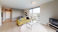 This contemporary single-floor residence showcases a thoughtfully designed open layout that maximizes both space and natural light. The living area serves as the heart of the home, featuring large floor-to-ceiling windows that frame expansive views of the surrounding urban landscape, allowing daylight to flood the interior. Light hardwood-style flooring runs consistently throughout, lending warmth and visual continuity to the space.

The kitchen is outfitted with modern flat-panel cabinetry in a warm wood-grain finish, light quartz countertops, a clean tile backsplash, and a full suite of stainless steel appliances including a gas range, built-in microwave, and undermount sink — offering both functionality and a refined aesthetic.

The bedrooms are serene and well-proportioned, each benefiting from large windows that provide ample natural light and city views. Sliding barn-style doors add a contemporary architectural touch, while the neutral palette creates a calm and restful atmosphere.

The bathroom is clean and efficiently designed, featuring a combined tub and shower with a curved rod, light tile surrounds, and wood-tone flooring. A dedicated laundry room with a side-by-side washer and dryer adds everyday convenience, completing this well-rounded and modern living space.
