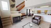This two-story home offers a thoughtfully designed layout that balances open communal spaces with comfortable private retreats. The main level centers around a spacious living room boasting soaring vaulted ceilings, soft carpeting, and a classic tiled fireplace that serves as a natural focal point. Large windows dressed with dark curtains draw in ample natural light, contributing to the room's bright and airy feel. A warm wood staircase with open railings connects the two floors, adding an architectural elegance to the space.

Adjacent to the living area, the dedicated dining space features track lighting overhead and windows that invite natural light, making it ideal for everyday meals or entertaining. The kitchen is equipped with wood-toned cabinetry, light countertops, and standard appliances, with a convenient pass-through connecting it to the living area. A doorway off the kitchen leads to an in-unit laundry area with built-in shelving for added storage.

Upstairs, the bedrooms offer a quiet, restful atmosphere with plush carpeting and vaulted ceiling details. The primary bedroom includes a spacious walk-in closet outfitted with wire shelving and multiple hanging rods. A full bathroom on this level features tile flooring, a tub-shower combination, and warm neutral wall tones, completing this well-appointed home.