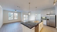 Located at 1750 FM-423 S in Little Elm, TX, this well-designed 2-bedroom, 2-bathroom residence offers a thoughtful single-floor layout with modern finishes throughout. The open-concept kitchen and living area serves as the heart of the home, anchored by a large center island topped with dark granite countertops, a stainless steel sink with a gold-tone faucet, and a built-in dishwasher. White shaker-style cabinetry lines the kitchen walls, complemented by a sleek tile backsplash and stainless steel appliances including a refrigerator, range, and microwave. Pendant lighting and track lighting illuminate the space, while light wood-style flooring flows seamlessly throughout. The living area is bright and airy, bathed in natural light from large windows and a glass door that opens to a generous private patio with open sky views. Each bedroom is comfortably sized, featuring ceiling fans, large windows with blinds, and light hardwood-style floors. The primary bedroom includes a walk-in closet with wrap-around shelving. The primary bathroom offers a dual-sink vanity with dark countertops, mosaic tile accents, and a walk-in shower. A hallway connects all rooms, completing this clean, contemporary residence.