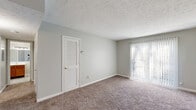 This single-floor unit is designed with a practical and cohesive layout, finished throughout in soft gray tones that lend a clean, neutral aesthetic. The living area is generously proportioned, featuring plush wall-to-wall carpeting and a textured ceiling. A large sliding glass door fitted with vertical blinds allows abundant natural light to enter while providing access to the outdoors. A louvered utility door adds a functional touch to the space.

The kitchen is outfitted with warm oak cabinetry, white appliances including a coil-burner electric range and a full-size refrigerator, and durable wood-look vinyl flooring. A pass-through opening connects the kitchen to the adjacent living area, enhancing the sense of openness. A ceiling fan is positioned overhead in the adjoining space.

The bedrooms are carpeted and finished in the same light gray palette. Each room benefits from natural light via windows with blinds, and storage is provided through closets with sliding or bifold panel doors. Ceiling fans are present in select rooms for added comfort.

The bathroom features wood-look vinyl flooring, a white tub-shower combination with a mounted shelf, and a standard toilet, all set within a compact and efficiently arranged space.