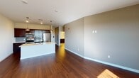 This well-appointed single-floor residence showcases a thoughtfully designed open-concept layout that seamlessly connects the kitchen and living areas. The kitchen is a standout feature, boasting rich dark-wood cabinetry with brushed nickel hardware, a large center island with a white quartz countertop and undermount sink, stainless steel appliances including a refrigerator, range, and built-in microwave, and stylish pendant lighting overhead. The living area flows naturally from the kitchen, featuring beautiful dark hardwood flooring and a large window that fills the space with abundant natural light and open outdoor views.

The bedrooms offer a comfortable, quieter retreat with soft wall-to-wall carpeting, neutral warm-toned walls, and windows that bring in generous natural light. The bathroom is clean and functional, featuring a full tub and shower combination with brushed nickel fixtures, a curved shower rod, and a dark-cabineted vanity with a white countertop, complemented by light tile flooring.

Throughout the residence, a consistent neutral color palette of warm beige and white tones creates a cohesive, inviting ambiance. Clean white baseboards, recessed lighting, and well-placed windows contribute to a bright, airy atmosphere that makes each room feel open and welcoming.