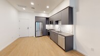 Located at 110 W Ocean Blvd in the heart of downtown Long Beach, California, this modern single-floor unit offers a sleek, contemporary design throughout. The open-concept kitchen is a standout feature, showcasing flat-front charcoal gray cabinetry, dark countertops, and a classic white subway tile backsplash. Stainless steel appliances — including a gas range, over-the-range microwave, French door refrigerator, and dishwasher — complete the fully equipped space. Light wood-style flooring runs throughout the kitchen and living areas, lending warmth to the clean, modern aesthetic. The bedroom is finished with plush neutral carpeting and features a large floor-to-ceiling window that fills the room with natural light and offers views of the surrounding urban landscape. The bathroom is thoughtfully designed with dual under-mount sinks set into a wide gray vanity with ample cabinetry, a large wall-to-wall mirror, light wood-style flooring, and a full bathtub with textured tile surround and built-in recessed shelving. Recessed lighting and crisp white walls throughout contribute to a bright, airy atmosphere, making this a polished and functional urban residence in one of Long Beach's most sought-after addresses.