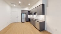 Located at 110 W Ocean Blvd in the heart of downtown Long Beach, California, this modern single-floor unit offers a sleek, contemporary design throughout. The open-concept kitchen is a standout feature, showcasing flat-front charcoal gray cabinetry, dark countertops, and a classic white subway tile backsplash. Stainless steel appliances — including a gas range, over-the-range microwave, French door refrigerator, and dishwasher — complete the fully equipped space. Light wood-style flooring runs throughout the kitchen and living areas, lending warmth to the clean, modern aesthetic. The bedroom is finished with plush neutral carpeting and features a large floor-to-ceiling window that fills the room with natural light and offers views of the surrounding urban landscape. The bathroom is thoughtfully designed with dual under-mount sinks set into a wide gray vanity with ample cabinetry, a large wall-to-wall mirror, light wood-style flooring, and a full bathtub with textured tile surround and built-in recessed shelving. Recessed lighting and crisp white walls throughout contribute to a bright, airy atmosphere, making this a polished and functional urban residence in one of Long Beach's most sought-after addresses.