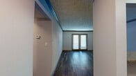 This single-floor, one-bedroom, one-bathroom unit offers a thoughtfully organized layout across a compact but functional footprint. The combined kitchen and living area serves as the heart of the home, featuring dark hardwood-style flooring, neutral gray walls, and a textured ceiling that adds visual depth. Crown molding accents the living space, which is anchored by a set of French doors that invite natural light and provide outdoor access. A pass-through counter connects the living area to the galley-style kitchen, which is equipped with dark espresso cabinetry, a white tile backsplash, granite-style countertops, stainless steel appliances including a full-size refrigerator, a dishwasher, and a range. Light wood-style flooring runs throughout the kitchen for easy maintenance. Two hallways connect the main living spaces to the private areas of the unit. The bedroom offers a comfortable amount of space with plush carpeting, neutral walls, a textured ceiling, and a window fitted with blinds for natural light control. The bathroom features wood-style flooring, a granite-topped vanity with dark cabinetry, and a tub and shower combination finished with earthy stone-look tile and mosaic accent detailing.