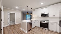 Located at 5672 Peachtree Pkwy in Peachtree Corners, GA, this well-appointed single-floor, 2-bedroom, 2-bathroom home offers a thoughtfully designed layout with modern finishes throughout. The heart of the home is the open-concept kitchen, showcasing crisp white shaker cabinetry, a white quartz peninsula island with an undermount sink, and a full suite of stainless steel appliances including a range, microwave, dishwasher, and French door refrigerator. Stylish pendant lighting with matte black accents hangs above the island, complementing the wood-look flooring that flows through the main living areas. Crown molding adds a refined touch to the common spaces. The two bedrooms are carpeted and filled with natural light from well-placed windows with blinds, offering a comfortable and quiet retreat. The primary bathroom features a glass-enclosed walk-in shower, white vanity cabinetry, and matte black hardware. The second bathroom includes a full tub-shower combo with matching black fixtures. A stacked washer and dryer unit is conveniently integrated into the hallway area. Two closets provide ample storage, and the overall neutral color palette creates a clean, welcoming ambiance throughout.