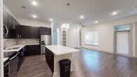 This single-story residence presents a thoughtfully designed open-concept layout that seamlessly connects the kitchen and living areas. The kitchen is a standout space, outfitted with dark espresso cabinetry, a light stone tile backsplash, and a full suite of stainless steel appliances including a range, microwave, dishwasher, and refrigerator with an ice dispenser. A generously sized center island with a crisp white countertop provides ample prep space and serves as a natural focal point. Pendant lighting illuminates the island, complementing the recessed lighting throughout. Rich wood-tone flooring extends across the main living area, where built-in shelving units flank the walls and a ceiling fan adds practical comfort. Natural light filters in through blinds-covered windows. The bedrooms feature plush carpeting and ceiling fans, while the bathrooms are finished with linear tile flooring and surround tile in the tub-shower combinations, accented by mosaic tile borders. The primary bathroom includes a dual-sink vanity with dark cabinetry and direct access to a spacious walk-in closet with built-in shelving and hanging rods. The overall aesthetic is clean and contemporary throughout.