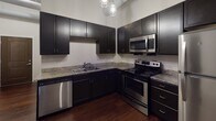 Located in the heart of downtown Fort Wayne, Indiana, this single-floor unit at 102 W Superior St blends industrial character with modern finishes throughout. The open main living area makes a strong first impression with rich, dark hardwood flooring that extends throughout the space, crisp white walls, and exposed ductwork along the ceiling that nods to the building's industrial heritage. Natural light filters in through horizontal windows fitted with blinds, lending the room an airy, loft-like atmosphere.

The kitchen is a standout feature, outfitted with sleek dark cabinetry that reaches toward the ceiling, providing generous storage. Granite countertops offer durable, attractive workspace, while a full suite of stainless steel appliances — including a refrigerator, electric range, built-in microwave, and dishwasher — ensures full functionality. Industrial-style pendant lighting above completes the kitchen's contemporary aesthetic.

The bathroom continues the cohesive design language with dark cabinetry topped by granite countertops, matching the kitchen's palette. Hardwood flooring carries through into the bath, and a clean, simply appointed shower and tub area rounds out the space. Overall, this unit offers a polished, urban living experience with thoughtful finishes and a well-connected downtown location.