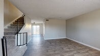 This two-story home offers a practical and comfortable layout spread across two well-defined levels, connected by a staircase with a classic metal railing. The main level features an open living and dining area with durable wood-look flooring, neutral gray walls, and textured ceilings throughout. A ceiling fan adds comfort to the living space, which leads to a sliding glass door providing outdoor access and natural light. The kitchen is equipped with dark espresso cabinetry, granite-look countertops, and black appliances including a range, microwave, and refrigerator, all set over warm hardwood-style flooring. A half bathroom on the main level provides added convenience for guests. Upstairs, multiple bedrooms are finished with plush carpeting, ceiling fans, and windows overlooking mature trees, lending a serene, natural feel to each room. Built-in closets with shelving offer practical storage in the bedrooms. A full bathroom on the upper level features a white vanity with a mirror, tile backsplash, and wood-look flooring. The consistent use of neutral tones, textured ceilings, and wood-look surfaces throughout creates a cohesive and inviting atmosphere across the entire home.