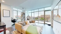 Located in Washington, DC's vibrant Shaw neighborhood, this modern one-bedroom, one-bathroom residence offers a thoughtfully designed layout with contemporary finishes throughout. The open-concept living and kitchen area is the centerpiece of the home, where dramatic floor-to-ceiling glass walls flood the space with natural light and frame expansive city views. Dark hardwood-style flooring anchors the living area, which offers direct access to an outdoor balcony. The kitchen is outfitted with flat-front wood cabinetry extending to the ceiling, stainless steel appliances, stone countertops, and a striking dark herringbone tile backsplash — a bold design detail that elevates the space. The bedroom is a calm retreat with large windows overlooking the cityscape, providing ample natural light. It connects directly to a well-organized walk-in closet featuring built-in shelving and hanging rods. The full bathroom features large-format porcelain tile flooring, white subway tile surrounding the soaking tub and shower, and a dark wood vanity. Clean lines, abundant natural light, and refined modern finishes define the overall ambiance of this well-appointed DC residence.