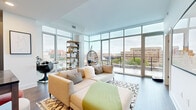 Located in Washington, DC's vibrant Shaw neighborhood, this modern one-bedroom, one-bathroom residence offers a thoughtfully designed layout with contemporary finishes throughout. The open-concept living and kitchen area is the centerpiece of the home, where dramatic floor-to-ceiling glass walls flood the space with natural light and frame expansive city views. Dark hardwood-style flooring anchors the living area, which offers direct access to an outdoor balcony. The kitchen is outfitted with flat-front wood cabinetry extending to the ceiling, stainless steel appliances, stone countertops, and a striking dark herringbone tile backsplash — a bold design detail that elevates the space. The bedroom is a calm retreat with large windows overlooking the cityscape, providing ample natural light. It connects directly to a well-organized walk-in closet featuring built-in shelving and hanging rods. The full bathroom features large-format porcelain tile flooring, white subway tile surrounding the soaking tub and shower, and a dark wood vanity. Clean lines, abundant natural light, and refined modern finishes define the overall ambiance of this well-appointed DC residence.