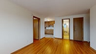 This single-floor unit offers a practical and well-organized layout with warm hardwood flooring that flows consistently throughout the main living areas and bedrooms, adding a sense of warmth and continuity to the space. The living area is open and bright, with windows that admit generous natural light and offer views of the surrounding urban streetscape. Baseboard heating runs along the walls, ensuring consistent comfort throughout the colder months.

The kitchen is a compact yet fully equipped space, featuring classic honey-toned wood cabinetry with ample upper and lower storage, light-toned countertops with a tile backsplash, and white appliances including an electric range and a full-size refrigerator. Tile flooring in the kitchen provides a clean contrast to the hardwood found elsewhere.

The bedrooms are well-proportioned and naturally lit, each with windows overlooking the exterior. One bedroom includes a ceiling fan and a window-mounted air conditioning unit for added climate control. Both rooms benefit from the same warm hardwood flooring found throughout the unit.

The bathroom is finished with classic cream-colored square tiles on the walls and a mosaic tile floor, and includes a full soaking tub, toilet, and a built-in recessed shelving unit. The overall aesthetic is functional and classic, offering a solid foundation for personalization.