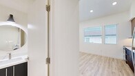 This two-floor studio in Chula Vista, California, offers a thoughtfully designed layout spread across two levels. Light wood-style flooring flows throughout both floors, creating a clean and cohesive aesthetic complemented by bright white walls and recessed lighting.

The main level houses a generously sized open area that serves as the primary living space, featuring soaring ceilings that enhance the sense of openness. Two kitchen areas are present — a standout feature of this unit. The main kitchen is fully equipped with stainless steel appliances, including a refrigerator, dishwasher, and range, paired with navy blue lower cabinetry, wood-tone upper cabinets, and white countertops. An adjacent area provides additional cabinetry and counter space, and the in-unit washer and dryer are conveniently integrated into this zone.

The bathroom is finished with a walk-in shower featuring built-in shelving, matte black fixtures, open wood shelving for storage, and light flooring that maintains the unit's clean palette.

The upper level provides an intimate secondary space bathed in natural light from multiple windows with blinds, and is equipped with a wall-mounted mini-split system for personalized climate control. A loft-style ladder connects the two floors, adding a distinctive architectural element to the studio's efficient and modern design.