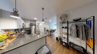 Located at 919 E Genesee Street in Syracuse, NY, this thoughtfully designed unit offers five bedrooms, four bathrooms, and a well-organized single-floor layout. The open-concept kitchen is a standout feature, outfitted with stainless steel appliances including a refrigerator, range, dishwasher, and microwave, complemented by granite-style countertops, two-tone cabinetry in white and gray, pendant lighting, and warm hardwood-style flooring. The kitchen flows naturally toward a hallway that connects the rest of the unit.

The living room is bright and welcoming, featuring a ceiling fan, light-toned flooring, and a large sliding glass door that fills the space with natural light and provides views of the surrounding cityscape. The bedrooms are comfortably sized, each featuring large windows with blinds and curtains to control natural light, ceiling fans, and neutral-toned walls. The spacious primary bedroom offers a serene retreat with ample room and city views. The four bathrooms are clean and modern, each equipped with a single vanity featuring granite-style countertops, dark cabinetry, a large mirror, and a shower-tub combination. A connecting hallway with hardwood-style flooring ties the rooms together in a cohesive, functional layout.