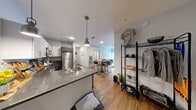 Located at 919 E Genesee Street in Syracuse, NY, this thoughtfully designed unit offers five bedrooms, four bathrooms, and a well-organized single-floor layout. The open-concept kitchen is a standout feature, outfitted with stainless steel appliances including a refrigerator, range, dishwasher, and microwave, complemented by granite-style countertops, two-tone cabinetry in white and gray, pendant lighting, and warm hardwood-style flooring. The kitchen flows naturally toward a hallway that connects the rest of the unit.

The living room is bright and welcoming, featuring a ceiling fan, light-toned flooring, and a large sliding glass door that fills the space with natural light and provides views of the surrounding cityscape. The bedrooms are comfortably sized, each featuring large windows with blinds and curtains to control natural light, ceiling fans, and neutral-toned walls. The spacious primary bedroom offers a serene retreat with ample room and city views. The four bathrooms are clean and modern, each equipped with a single vanity featuring granite-style countertops, dark cabinetry, a large mirror, and a shower-tub combination. A connecting hallway with hardwood-style flooring ties the rooms together in a cohesive, functional layout.