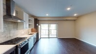Located in the Linden Hills neighborhood of Minneapolis, this single-floor residence offers a thoughtfully designed open-concept layout with upscale finishes throughout. Rich dark hardwood flooring flows seamlessly through the main living area, anchored by recessed lighting and a soft, neutral color palette that creates a clean and contemporary ambiance.

The kitchen is a standout feature, showcasing a mix of white shaker and dark wood cabinetry, white quartz countertops, and a stone tile backsplash. Stainless steel appliances include a gas range with a stainless steel hood, a built-in microwave, dishwasher, and refrigerator. A sliding glass door off the main living area opens to an outdoor balcony, flooding the space with natural light and providing views of the surrounding neighborhood.

A carpeted bedroom offers a tranquil retreat with a large window overlooking tree-lined surroundings. A dedicated laundry area includes a stacked washer and dryer alongside a custom built-in shelving and drawer system for organized storage. The bathroom features large-format tile flooring, a dark wood vanity with white countertop, and a tiled tub-shower combination. The unit also includes a well-lit entry foyer with a wood door and elegant overhead fixture.