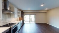 Located in the Linden Hills neighborhood of Minneapolis, this single-floor residence offers a thoughtfully designed open-concept layout with upscale finishes throughout. Rich dark hardwood flooring flows seamlessly through the main living area, anchored by recessed lighting and a soft, neutral color palette that creates a clean and contemporary ambiance.

The kitchen is a standout feature, showcasing a mix of white shaker and dark wood cabinetry, white quartz countertops, and a stone tile backsplash. Stainless steel appliances include a gas range with a stainless steel hood, a built-in microwave, dishwasher, and refrigerator. A sliding glass door off the main living area opens to an outdoor balcony, flooding the space with natural light and providing views of the surrounding neighborhood.

A carpeted bedroom offers a tranquil retreat with a large window overlooking tree-lined surroundings. A dedicated laundry area includes a stacked washer and dryer alongside a custom built-in shelving and drawer system for organized storage. The bathroom features large-format tile flooring, a dark wood vanity with white countertop, and a tiled tub-shower combination. The unit also includes a well-lit entry foyer with a wood door and elegant overhead fixture.