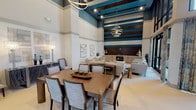 Located on Mira Lago Blvd in Farmers Branch, Texas, this single-story clubhouse presents a striking interior defined by its dramatic double-height ceilings and bold design choices. The main gathering area immediately commands attention with its teal-painted upper walls accented by horizontal dark wood beams, creating a visually dynamic focal point that anchors the entire space.

The open-plan layout seamlessly integrates distinct functional zones. A dining area features a substantial wood table surrounded by upholstered chairs, positioned beneath sculptural orbital chandeliers that add a contemporary, artistic touch. Adjacent lounge seating areas are furnished with neutral-toned sofas and accent chairs arranged around a round wood coffee table, complemented by a built-in media console below the statement wall.

A separate lounge zone showcases a stunning floor-to-ceiling marble slab wall backdrop framing a full wet bar with counter seating, reinforcing the upscale character of the space. Patterned lounge chairs flank the bar area, offering additional social seating.

Large floor-to-ceiling glass doors and windows flood the interior with abundant natural light and provide direct outdoor views and access to an exterior terrace. Light-toned tile flooring flows consistently throughout, enhancing the sense of openness and cohesion across this refined communal space.