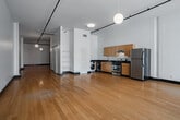 Located at 620 S Main St in the heart of Downtown Los Angeles, this single-floor unit offers a clean, contemporary design with an open and airy layout. Warm-toned hardwood flooring runs throughout the main living areas, complementing the crisp white walls and contrasting dark baseboards that define the space's modern aesthetic. Track lighting spans the length of the ceiling, providing flexible illumination across the expansive open floor plan.

The living area is bathed in natural light through large floor-to-ceiling windows that frame sweeping views of the Downtown LA skyline, with globe pendant lights adding a stylish accent overhead. Built-in shelving provides convenient storage along one wall, and a frosted glass interior door contributes to the space's clean, minimalist character.

The kitchen is well-appointed with warm wood cabinetry, dark granite countertops, a double stainless steel sink, a gas range with overhead ventilation, and a full-size stainless steel refrigerator — offering a functional and attractive cooking environment.

The bathroom features a classic black-and-white tiled tub-shower combination with a handheld showerhead and deep navy floor tiles, delivering a bold, graphic contrast to the otherwise neutral palette of the unit. Overall, the space presents a polished urban living environment in one of Los Angeles's most vibrant neighborhoods.