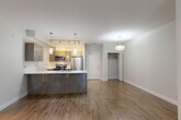 Located in Langley, BC, this 2-bedroom, 2-bathroom apartment offers a thoughtfully designed open-concept layout across a single floor. The living and dining area is finished with warm wood-tone laminate flooring and features sliding glass doors that open onto a private balcony, filling the space with natural light and providing outdoor views of the surrounding community.

The kitchen is a standout feature, showcasing a large central island with a white quartz countertop and undermount sink, dark wood cabinetry, warm-toned upper cabinets, and a full suite of stainless steel appliances including a refrigerator, range, and microwave. Pendant lighting and a track lighting system complete the modern aesthetic.

Both bedrooms are carpeted and offer a calm, neutral palette, with the primary bedroom including its own closet with built-in shelving. The second bedroom is equally well-sized and versatile. Each bathroom is finished with tile flooring, a sliding glass shower enclosure, and a vanity with a stone-finish countertop and large mirror.

Additional features include two closets, an in-unit laundry area with a stacked Whirlpool washer and dryer, and baseboard heating throughout. The overall design is clean, contemporary, and functional.