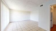 This single-floor, one-bedroom, one-bathroom unit is thoughtfully laid out to maximize functionality and comfort. The living area is a standout feature, showcasing a distinctive white-painted brick accent wall that adds texture and character to the space. Light tile flooring flows throughout the common areas, while a large sliding glass door fitted with vertical blinds allows natural light to pour in and provides access to the outdoors. A ceiling fan is also present in the living area, contributing to year-round comfort. The kitchen is efficiently designed with white cabinetry, generous countertop space, a stainless steel sink, and a warm earth-toned tile backsplash that adds a touch of color. A textured popcorn ceiling is consistent throughout the unit. The bedroom is finished with plush wall-to-wall carpeting, offering a softer, more comfortable feel, and features a sliding-door closet with built-in shelving and a hanging rod for organized storage. The bathroom includes a full tub-shower combination with clean white tile surround. Overall, the unit presents a straightforward, well-maintained layout suited for everyday living.