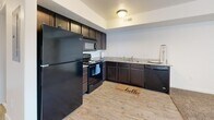 Located at 149 E Vine St in Murray, Utah, this efficiently designed single-floor unit offers a thoughtful layout that maximizes every square foot. The open-concept kitchen and living area serves as the heart of the space, with the kitchen featuring dark espresso cabinetry, granite-style countertops, a full suite of black appliances including a refrigerator, range, built-in microwave, and dishwasher, all set atop durable wood-look flooring. The living area transitions seamlessly from the kitchen, offering plush carpeting and a large sliding glass door with vertical blinds that invites natural light and provides outdoor access. The hallway connects the main living space to the full bathroom, which is appointed with a dark vanity, granite-style countertop, a tub-shower combination, and tile flooring. A standout convenience feature of this unit is the in-unit stacked washer and dryer, neatly tucked into the hallway alcove alongside the electrical panel. The unit's neutral color palette of warm whites and beige tones throughout creates a clean, versatile ambiance suited to a variety of décor styles. This well-appointed unit offers a practical and comfortable living environment in a convenient Murray location.