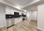 Located at 10119 85 Ave NW, this thoughtfully designed single-floor suite makes efficient use of its compact footprint. The space is finished to a modern standard, with light-toned luxury vinyl plank flooring running throughout, crisp white walls, and recessed pot lighting that keeps the interior bright and welcoming.

The kitchen is a standout feature, outfitted with full-height white shaker cabinetry accented by matte black hardware and a striking dark tile backsplash. A complete suite of stainless steel appliances — including a French door refrigerator, electric range, over-the-range microwave, and dishwasher — provides full functionality. Grey countertops and a single-basin undermount sink complete the clean, contemporary look. The open layout allows the kitchen to flow naturally into the living area, which benefits from ground-level windows that invite natural light.

The bathroom is finished with large-format grey tile on both the floors and tub surround, lending a spa-like quality to the space. White cabinetry with open shelving, dark hardware, and a grey countertop with a vessel-style sink tie the room's aesthetic together cohesively. A full soaking tub rounds out the bathroom's amenities. Overall, the suite presents a polished, move-in-ready interior with consistent, modern finishes throughout.