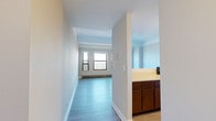 Located along North Stockton Drive in Chicago's Lincoln Park neighborhood, this single-floor unit offers a well-organized layout with distinct living, sleeping, and kitchen areas connected by a central hallway. Light-toned hardwood-style flooring runs throughout the main living and common areas, while carpeting provides a softer feel in the bedroom spaces. Baseboard heating units are present throughout, ensuring consistent warmth across all rooms.

The main living area is generously proportioned, featuring large windows with black frames that frame expansive views, likely toward Lake Michigan and the surrounding parkland. Structural beam details and crown molding add architectural character to the ceiling. An additional room, suitable as a bedroom or secondary living space, features its own windows with exterior views and ceiling fan.

The kitchen is equipped with stainless steel appliances including a refrigerator, dishwasher, and range, complemented by dark wood cabinetry offering ample storage and light-toned countertops. A second, more traditional kitchen configuration is also visible in images, featuring warm wood cabinetry and hardwood-style flooring. Bedroom areas include closets with built-in shelving and hanging rods. The overall ambiance is clean, neutral, and move-in ready.