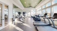 Located at 225 Rhyne Rd in Charlotte, NC, this fitness center is designed to support a comprehensive workout experience within a bright, thoughtfully appointed single-floor space. The room's architectural design draws immediate attention with its distinctive tray ceiling, finished in a bold green accent that contrasts cleanly against white walls and recessed lighting. A ceiling fan is centrally mounted within the tray, contributing to air circulation throughout the facility.

Large, multi-pane windows line multiple walls, flooding the interior with abundant natural light and providing outdoor views of the surrounding property. The generous window placement creates an open, airy atmosphere that enhances the overall exercise environment. Durable speckled rubber flooring covers the workout area, providing both traction and cushioning underfoot.

The cardio zone is well-stocked with a row of treadmills, elliptical trainers, stationary cycles, and a stair climber—primarily TRUE Fitness branded equipment. A dedicated strength training area includes a full dumbbell rack with a wide weight range, a cable machine with an adjustable bench, and medicine balls stored on a nearby rack. Floor-to-ceiling mirrors along one wall expand the visual space and allow users to monitor their form. The overall ambiance is clean, modern, and energizing.