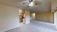 This single-floor unit offers a functional and comfortable layout with warm, neutral cream-toned walls and plush gray carpeting throughout the living and bedroom areas. The open living room is generously proportioned, highlighted by a ceiling fan with a light fixture and a large sliding glass door that fills the space with natural light and provides views of outdoor greenery. The kitchen is efficiently designed with warm wood cabinetry, dark laminate countertops, and tile flooring. It is fully equipped with white appliances including a gas range, dishwasher, and refrigerator, offering ample counter and storage space. Conveniently positioned adjacent to the kitchen is a dedicated in-unit laundry area with a stacked washer and dryer. The unit includes two bedrooms, each featuring plush carpeting and closet storage — one with a walk-in closet and one with an open built-in closet. Two bathrooms serve the unit, each with tile flooring, a wood-toned vanity, white countertop, and a large wall mirror. The overall ambiance is clean, practical, and move-in ready, with a consistent neutral palette throughout.