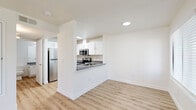 Located at 7803 W Deschutes Ave in Kennewick, Washington, this one-bedroom, one-bathroom unit offers a well-organized single-floor layout designed for comfortable everyday living. The combined kitchen and living area forms the heart of the home, featuring light wood-style flooring that flows throughout the entire unit. The kitchen is outfitted with white shaker-style cabinetry, dark granite-style countertops, stainless steel appliances including a refrigerator, electric range, and microwave, and a peninsula with a built-in sink that opens toward the living space. The living room is bright and welcoming, filled with natural light from a large sliding glass door fitted with vertical blinds and an adjacent window. A tile-surround fireplace with a classic mantel adds a distinctive focal point to the living area. The generously sized bedroom features a window overlooking the surroundings and connects to a hallway with access to a dedicated closet. The full bathroom includes a white vanity with dark countertops, a large mirror with overhead lighting, and a shower-tub combination. Clean white walls, consistent flooring, and recessed lighting throughout contribute to a bright, cohesive aesthetic.