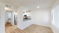 Located at 7803 W Deschutes Ave in Kennewick, Washington, this one-bedroom, one-bathroom unit offers a well-organized single-floor layout designed for comfortable everyday living. The combined kitchen and living area forms the heart of the home, featuring light wood-style flooring that flows throughout the entire unit. The kitchen is outfitted with white shaker-style cabinetry, dark granite-style countertops, stainless steel appliances including a refrigerator, electric range, and microwave, and a peninsula with a built-in sink that opens toward the living space. The living room is bright and welcoming, filled with natural light from a large sliding glass door fitted with vertical blinds and an adjacent window. A tile-surround fireplace with a classic mantel adds a distinctive focal point to the living area. The generously sized bedroom features a window overlooking the surroundings and connects to a hallway with access to a dedicated closet. The full bathroom includes a white vanity with dark countertops, a large mirror with overhead lighting, and a shower-tub combination. Clean white walls, consistent flooring, and recessed lighting throughout contribute to a bright, cohesive aesthetic.