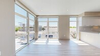 This modern residence in Roseville, CA offers a thoughtfully designed single-floor layout with three bedrooms and two bathrooms. Light wood-tone flooring runs throughout, creating a cohesive and airy feel that complements the neutral warm-beige walls and clean white trim.

The living area is a standout feature, boasting expansive floor-to-ceiling windows and glass doors on two walls that flood the space with natural light and frame open city views. The kitchen is sleek and contemporary, featuring a large center island with a white quartz countertop, two-toned cabinetry in white and dark charcoal gray, stainless steel appliances including a built-in wall oven and French door refrigerator, and a window that brings in additional natural light.

The bedrooms are well-proportioned, each offering generous windows with outdoor views and ample closet space. The primary bedroom includes a spacious walk-in closet with custom built-in shelving. Additional bedrooms feature sliding-door closets with built-in organization. A mini-split HVAC unit is present in one of the secondary bedrooms for personalized climate control.

The bathrooms are finished in a modern style, with one featuring a floating dark-cabinetry vanity, vessel sink, and an illuminated LED mirror. A bright, clean hallway with recessed lighting connects all areas of the home, enhancing the overall sense of openness and flow.
