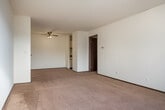 This single-floor residential unit offers a practical and comfortable layout designed to maximize everyday functionality. The living area is carpeted in a warm neutral tone and features a ceiling fan with integrated lighting, providing both comfort and airflow. Natural light filters in through vertical-blind-covered windows, brightening the space and creating an inviting atmosphere. Baseboard heating runs along the perimeter of the carpeted rooms, ensuring consistent warmth throughout.

The kitchen is efficiently appointed with cream-colored cabinetry featuring dark trim, dark laminate countertops, and a double stainless steel sink. Tile flooring and under-cabinet lighting add practical touches to the cooking space.

The bathroom is well-equipped with a wooden vanity cabinet topped by a white countertop and mirror, mosaic tile flooring, and a full tub-shower combination enclosed by floor-to-ceiling beige square tiles.

Storage is a notable feature of this unit, with a large built-in closet offering hanging rods and multiple shelving units, providing ample organization space. The overall layout, as seen in the dollhouse view, includes multiple rooms connected by a clear and logical flow, making this a well-structured and livable space.