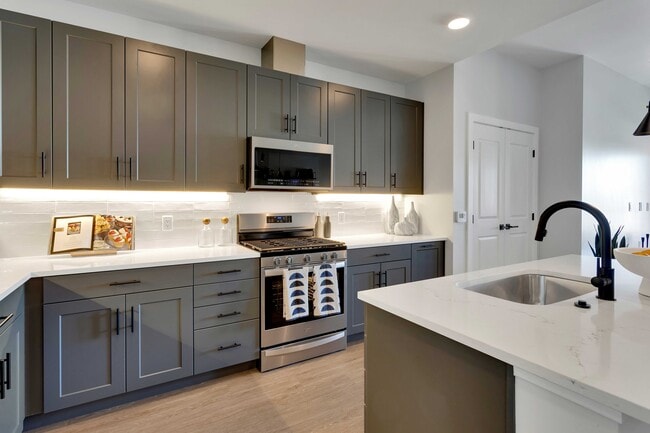 Modern kitchen with sleek grey cabinets, stainless steel appliances, and elegant white countertops, featuring a stylish island sink. - The Fitzgerald