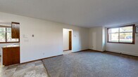 Located at 2052 15th St N in Saint Cloud, Minnesota, this single-floor, 3-bedroom, 1-bathroom residence offers a practical and efficiently arranged layout. The living area features a combination of tile and plush carpet flooring, neutral white walls, wood trim accents, and a textured ceiling, creating a clean and straightforward aesthetic throughout. Baseboard heating is present in multiple rooms, providing consistent warmth during Minnesota's colder months.

The kitchen is well-equipped with warm wood cabinetry, a double-basin sink, laminate countertops, and white appliances including a range and refrigerator. A window above the sink overlooks a lush, tree-lined exterior, bringing in natural light and pleasant outdoor views. The tile flooring continues throughout the kitchen for easy maintenance.

The spacious primary bedroom is notably generous in size, offering ample room for furnishings, and includes access to a closet. The two additional bedrooms are carpeted and well-proportioned, each with warm wood-trimmed doors and baseboard heating. The full bathroom features a tub-shower combo with a clean, neutral surround and standard fixtures. A connecting hallway ties the bedrooms, bathroom, and living areas together in a cohesive and accessible flow.