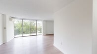 Located on the fourth floor at 101 S Whiting St in Alexandria, Virginia, this well-appointed unit offers a clean, modern aesthetic throughout its thoughtfully organized single-level layout. The living room is a standout feature, anchored by expansive floor-to-ceiling sliding glass doors that flood the space with natural light and provide direct access to a private balcony. From the balcony, residents enjoy open views of mature tree canopies, manicured greenery, and the surrounding Alexandria streetscape, with city buildings visible in the distance. Light wood-tone flooring runs consistently throughout the interior, complementing the crisp white walls and textured ceilings to create a bright, airy atmosphere. A wall-mounted mini-split HVAC unit ensures climate comfort year-round. The unit includes two bathrooms, one of which features light tile flooring, a tub-shower combination with white tile surround, and granite countertop finishes. Additional rooms provide flexible living or sleeping arrangements, each finished with the same clean hardwood-style flooring. A dedicated closet offers practical storage. The overall design is minimal and move-in ready, with a neutral palette that suits a variety of interior styles. This residence combines functional urban living with a serene, light-filled environment in a well-established Alexandria neighborhood.