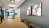 Located at 2206 Ellsworth Blvd in Ballston Spa, NY, this single-floor amenity center offers a generously sized, thoughtfully designed space built to serve a modern residential community. The welcoming lobby greets visitors with striking herringbone-patterned hardwood flooring, bold teal accent walls, circular pendant lighting, and glass-panel entryways that invite natural light and views of the surrounding neighborhood.

The expansive fitness center is a standout feature, offering a wide range of Life Fitness cardio equipment — including treadmills, ellipticals, and stair climbers — alongside a comprehensive strength training area with free weights, cable machines, and wall-mounted mirrors. The gym benefits from an exposed black ceiling with sleek linear lighting and large windows that bring in natural light and outdoor views. A dedicated golf simulator room provides a unique recreational offering, complete with a full turf floor and a high-definition projection screen.

The communal lounge area features a curved, plush sectional sofa, track lighting, and curated artwork, creating an inviting space for relaxation and social interaction. The dining and kitchen area includes a long communal table, warm pendant lighting, open shelving, a full refrigerator, and large windows overlooking the streetscape — ideal for gatherings and events. Together, these spaces create a well-rounded, amenity-rich environment.