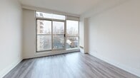 Located at 50 Spadina Rd in Toronto's Annex neighbourhood, this two-level, 1-bedroom, 2-bathroom unit offers a well-organized layout split evenly across two floors, connected by a white-railed staircase. Light hardwood-style flooring runs throughout, complementing the crisp white walls and clean aesthetic.

The main level features an entrance with a hallway leading into an open-concept combined dining and living area, flooded with natural light through floor-to-ceiling windows that frame sweeping views of the Toronto skyline and surrounding neighbourhood. The modern kitchen is outfitted with white shaker cabinetry, a grey quartz peninsula with a double undermount sink, subway tile backsplash, and stainless steel appliances including a range, over-the-range microwave, dishwasher, and refrigerator. A full bathroom and in-unit laundry are also found on this level.

The upper floor hosts the private bedroom, a versatile den, a second full bathroom with white tile flooring and vanity, and four closets offering generous storage. The bedroom features a mirrored sliding closet and a window with city views. Both bathrooms are finished in clean white tones with chrome fixtures. The overall ambiance is bright, functional, and modern throughout.